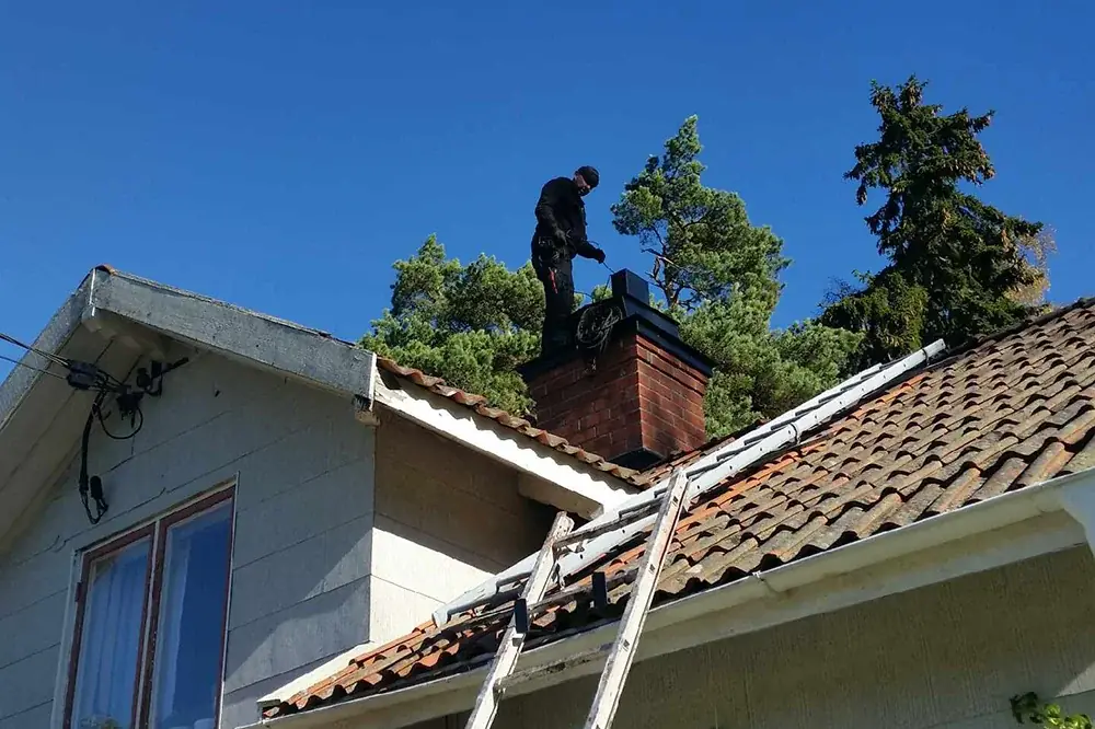 Sotare på husets tak vid skorstenen med stege uppställd mot takfoten